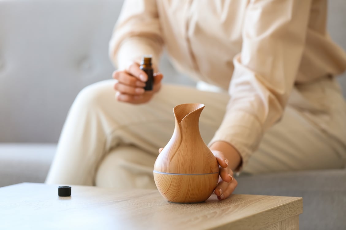 Female Hand Holding Essential Oil Diffuser on Wooden Table, Closeup